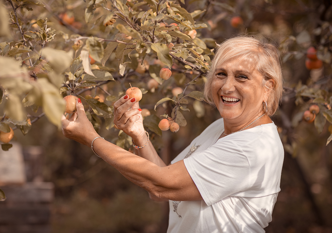 Natural Pharmaceuticals Imuberin® Mosolygó nő almaszedés közben lombos almafa alatt, ősz alapszínekkel.