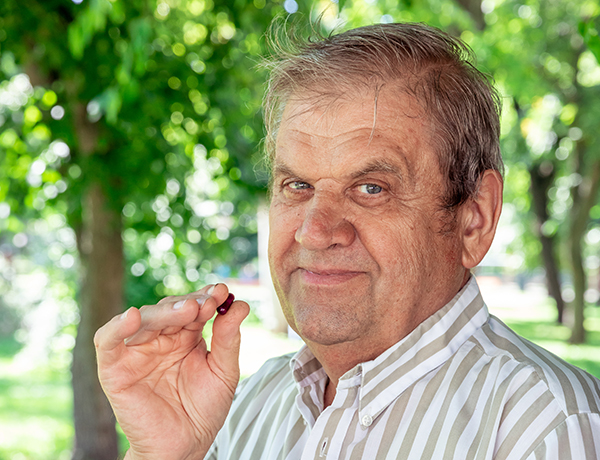 Natural Pharmaceuticals Imuberin® Egy középkorú férfi természetes környezetben, kezében egy lila Imuberin® kapszulát tart.