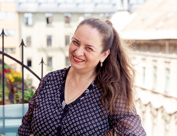 Natural Pharmaceuticals Imuberin® Mosolygós nő laza mintás blúzban erkélyen egy városi háztetők között napfényben.