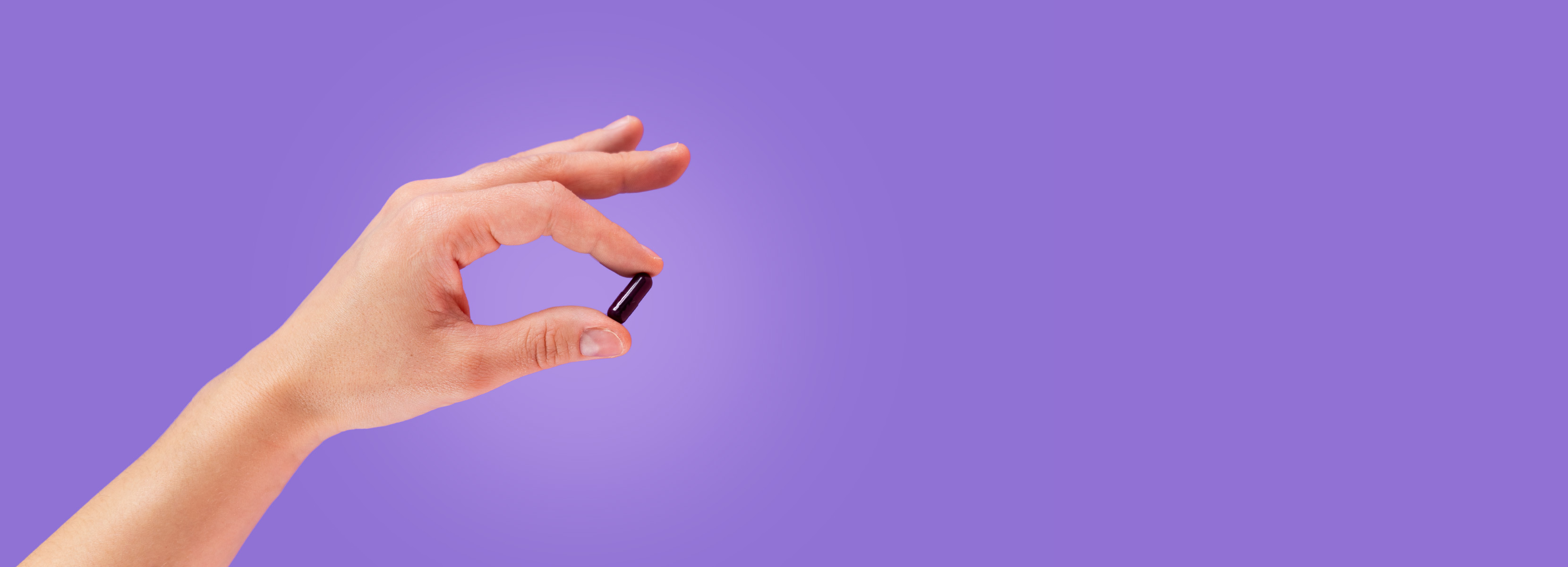 Natural Pharmaceuticals ImuBerin Kéz, amely egy lila ImuBerin kapszulát tart rózsaszín háttér előtt.